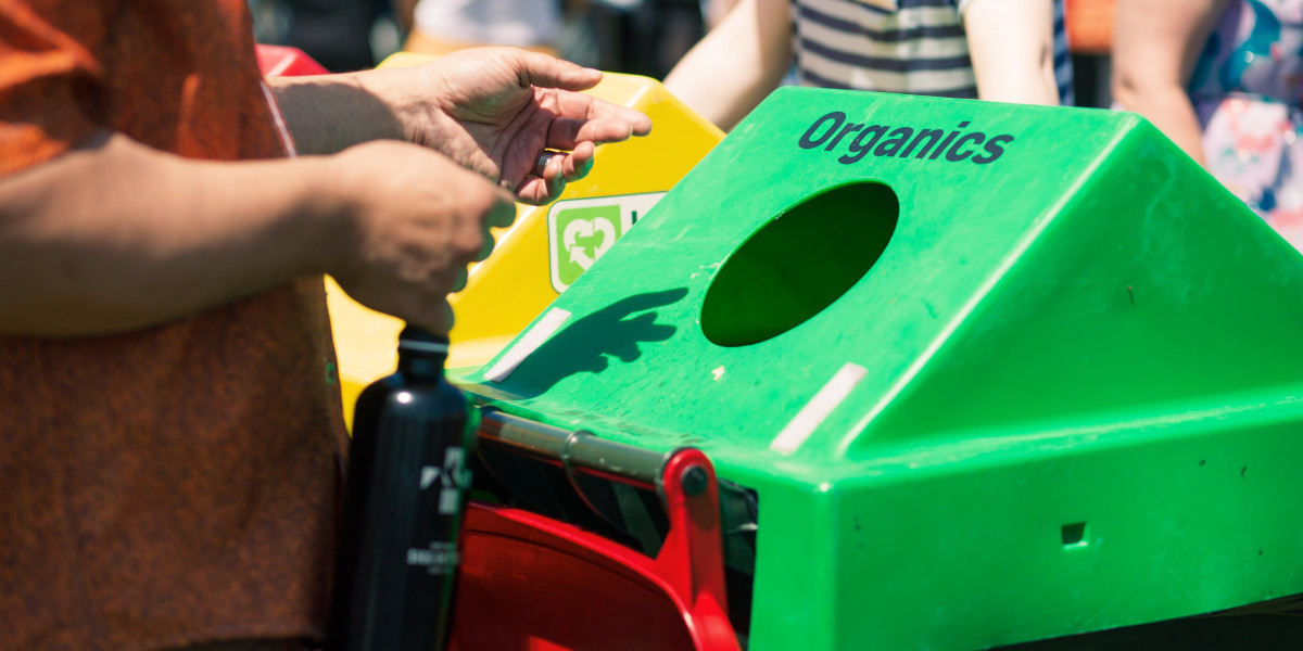 Person standing next to a green organics waste bin