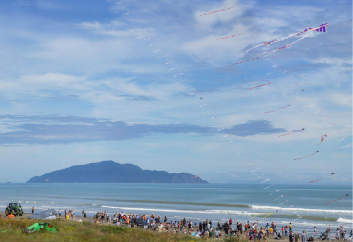 People at Ōtaki Beach enjoying the Ōtaki Kite Festival with Kāpiti Island in the background.