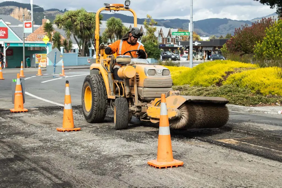 Road worker on a roller rolling out road path with cones in the foreground