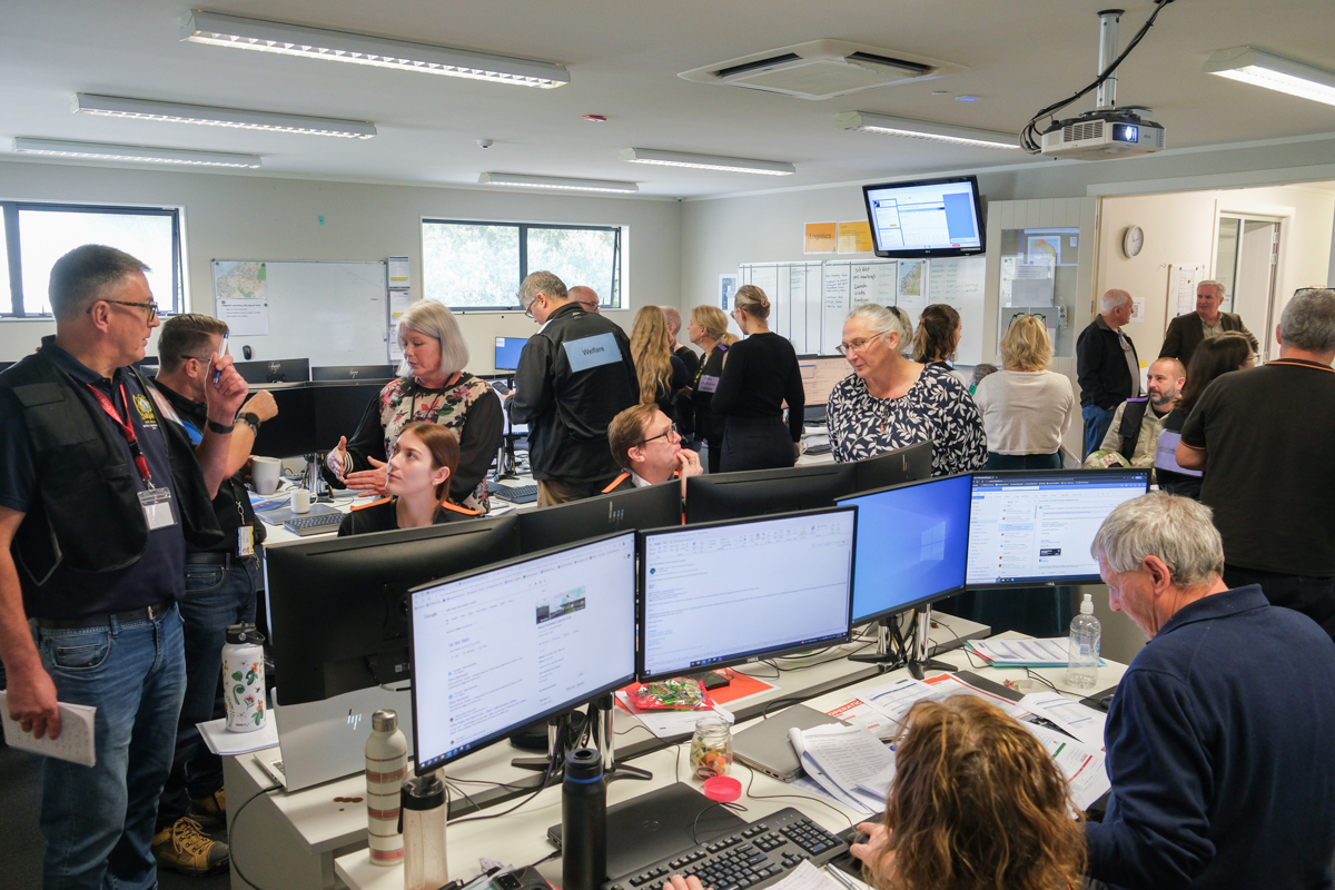 Staff busy in the Emergency Operations Centre working on screens and conversing with each other.