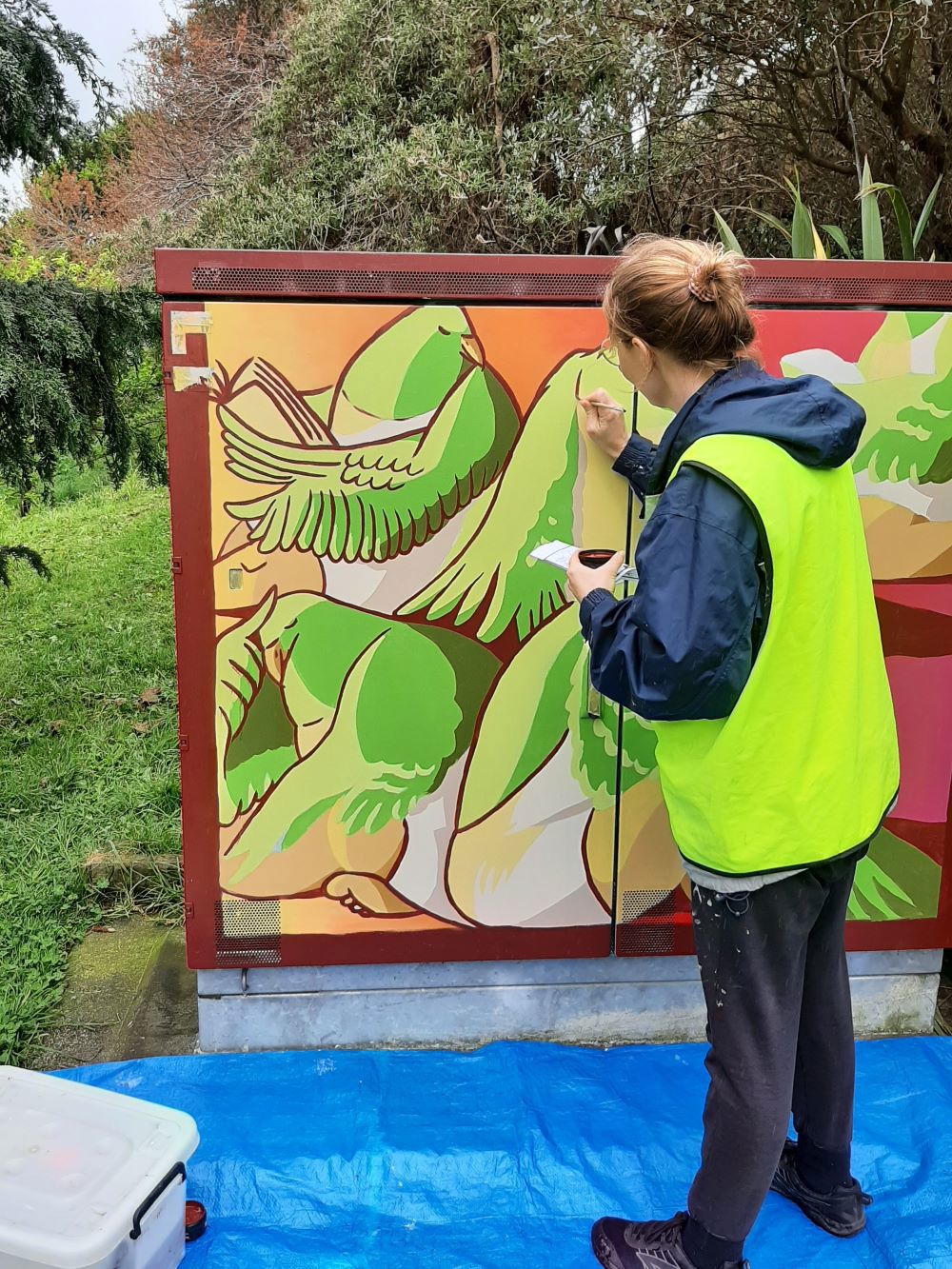 Local artist Ruth Michener in action painting a mural on a Chorus cabinet in Raumati
