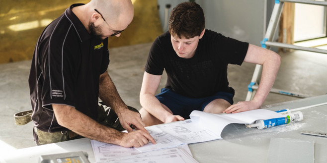 A builder and teenage helper looking at construction plans while completing an internship programme