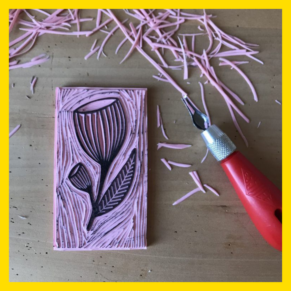 A pink stamp showing a flower carved from lino, surrounded by pink lino shavings and a carving tool