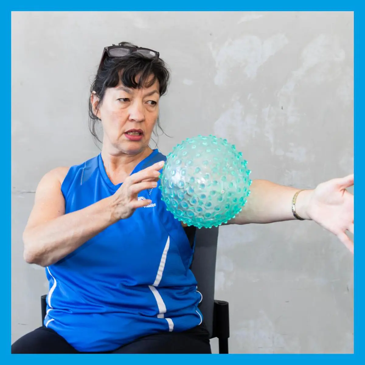 Instructor sitting on a chair doing some arm exercises using a ball.