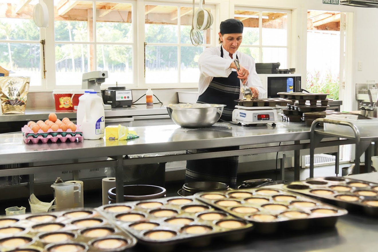 Photo showing a chef at work in a kitchen, with trays of food in the foreground
