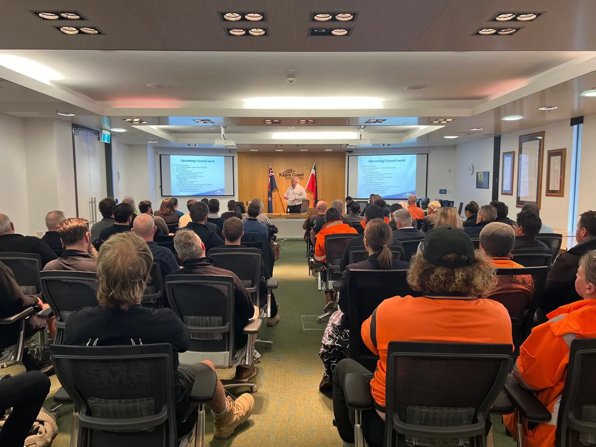 A collection of people observing a speaker with a slideshow presentation 