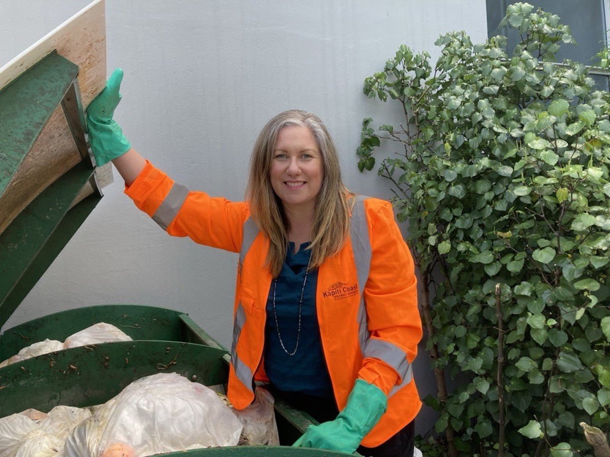 Kāpiti Coast District Council's climate action and connected communities manager Monique Engelen wearing an orange high vis jacket and gloves opening a waste bin.