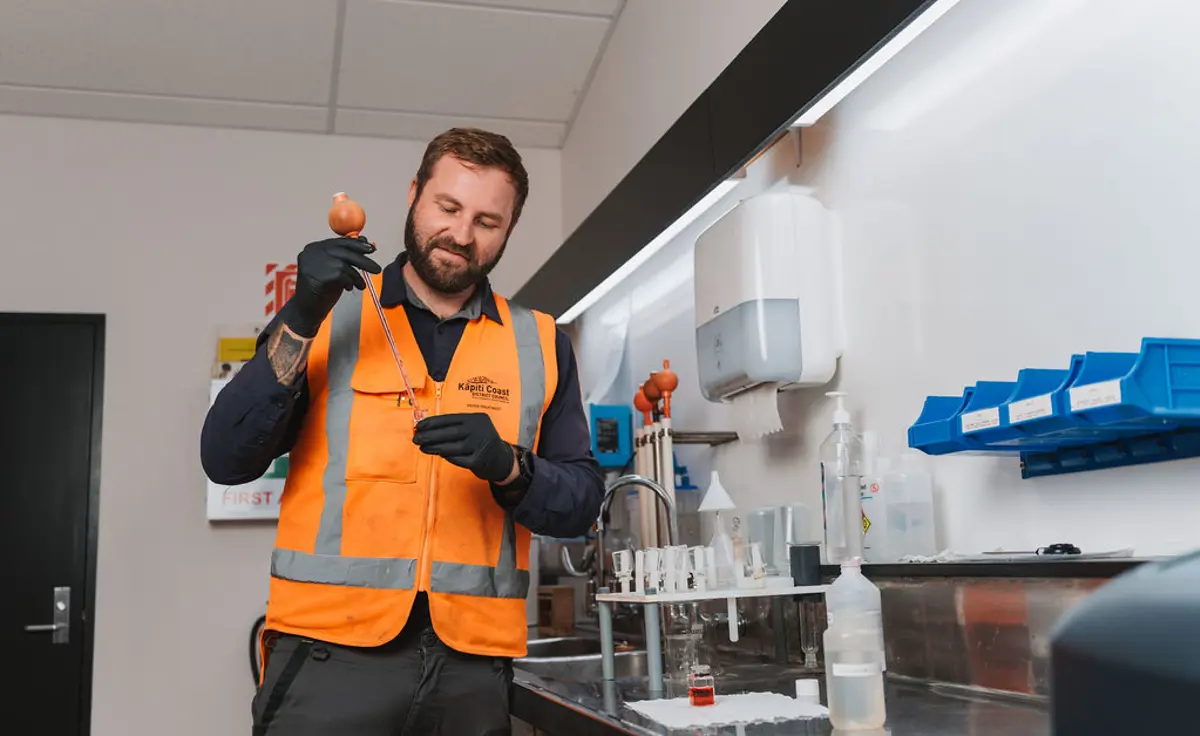 Kāpiti coast worker in high a high vis vest testing the water quality of drinking water. He has a test tube and a pipette  