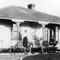 Mr and Mrs Heffer on the verandah of their home in Paraparaumu, ca 1908. Mr Heffer was the village blacksmith. He is pushing a (ca 1906) Douglas motorcycle with a wickerwork sidecar, the other motorcycle is of the same vintage Hp 321, Howell Collection thumbnail
