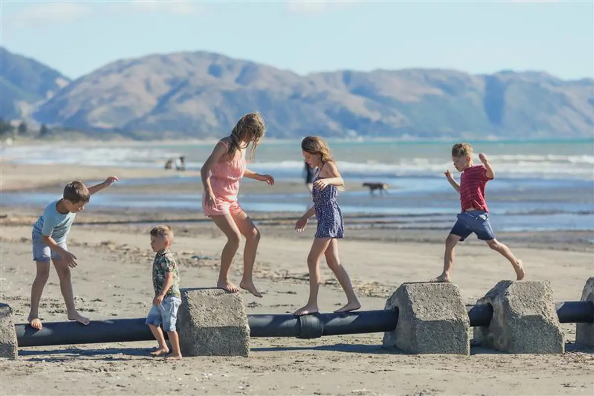 Children playing on the concrete blocks of a stormwater pipe at Raumati Beach