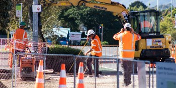 Photo of people in hi-viz safety clothing working on a road, with a digger in the background.