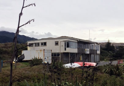 Image showing a view of the Paekākāriki Surf Club clubrooms, with flax in the foreground and surf boats stored beside