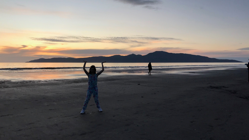 People playing on Paraparaumu Beach at dusk, with Kāpiti Island in the background.
