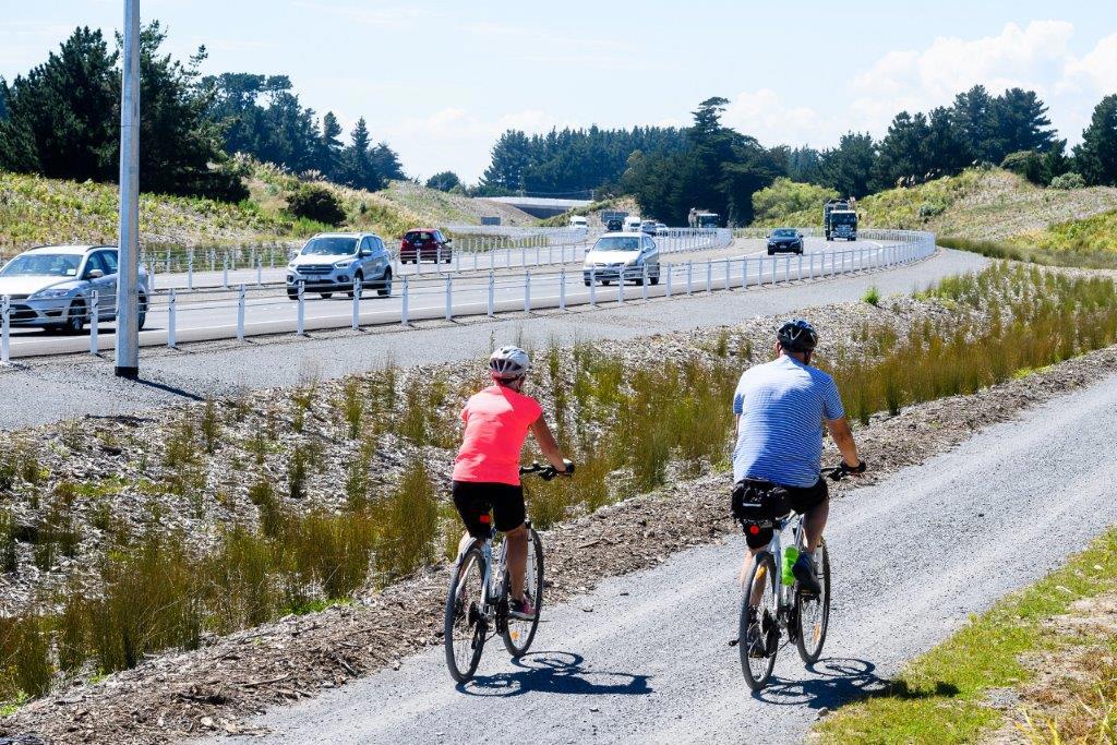 Two cyclists on the Kāpiti Expressway shared pathway with vehicles on the Expressway in the background.
