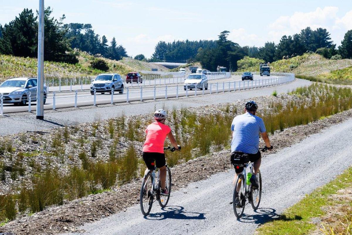 Two cyclists on the Kāpiti Expressway shared pathway with vehicles on the Expressway in the background.